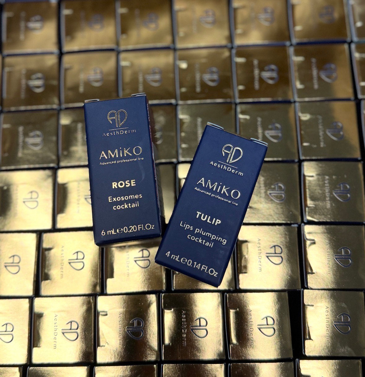 Two blue cosmetic containers labeled 'Amiko' on a background of gold boxes.